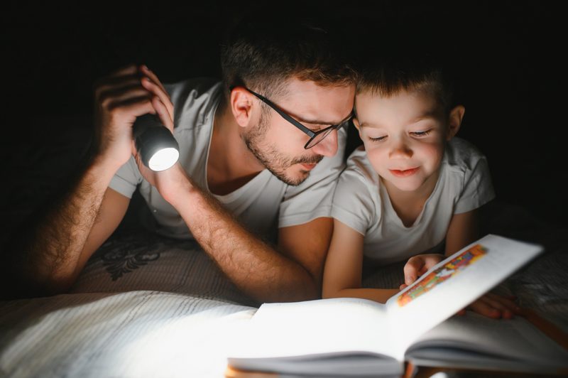 Vater und Sohn lesen abends unter der Decke